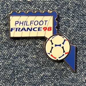 May include: A blue and white enamel pin with a soccer ball and the text "PHILFOOT FRANCE 98".