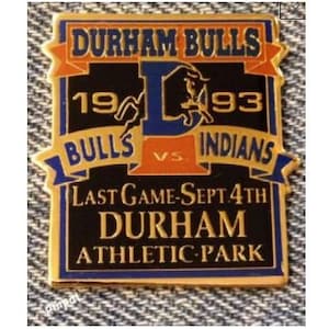 May include: A gold-coloured pin with a black background. The pin features the text "DURHAM BULLS" in a red banner at the top, with the years "19" and "93" on either side of a blue "P". Below the "P" is a banner with the text "BULLS VS INDIANS". The bottom of the pin features the text "LAST GAME-SEPT 4TH DURHAM ATHLETIC PARK".