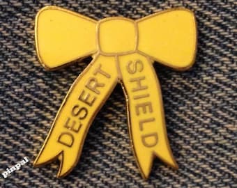 May include: A yellow bow with the words "Desert Shield" written on it.