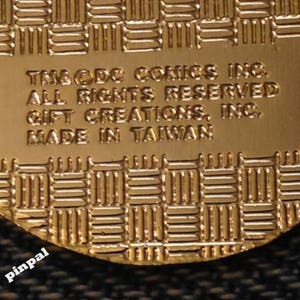 May include: Close-up of a gold-colored metal pin with the text "TM & DC COMICS INC. ALL RIGHTS RESERVED GIFT CREATIONS, INC. MADE IN TAIWAN" on the back.