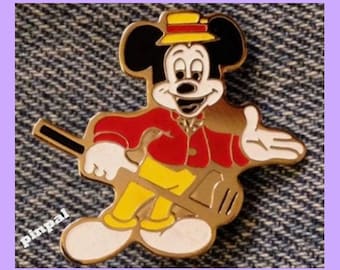 May include: A gold-colored pin featuring Mickey Mouse dressed in a red jacket, yellow pants, and a yellow hat. He is holding a golf club and smiling.