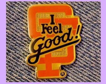 May include: A gold and orange enamel pin with the text "I Feel Good!" in black lettering. The pin has a registered trademark symbol.