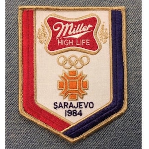 May include: A red, white, and blue embroidered patch with the Miller High Life logo, Olympic rings, and the text "Sarajevo 1984".