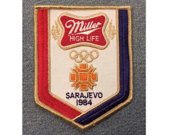 May include: A red, white, and blue embroidered patch with the Miller High Life logo, Olympic rings, and the text "Sarajevo 1984".