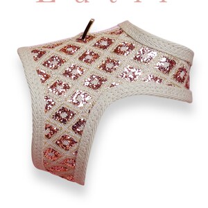 May include: A beige dog harness with a pink and gold glitter diamond pattern. The harness has a gold metal clip.