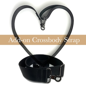 May include: Black adjustable crossbody strap with silver hardware. The strap is shown in a heart shape, with the ends of the strap forming the top of the heart.