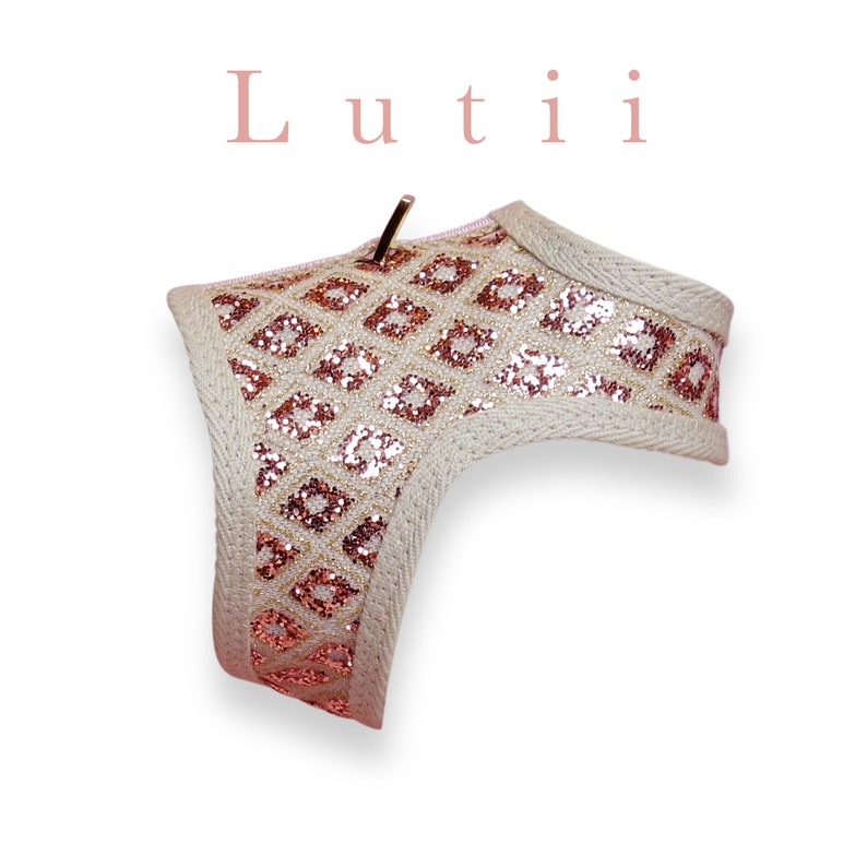 May include: A beige dog harness with a pink and gold glitter diamond pattern. The harness has a gold metal clip.