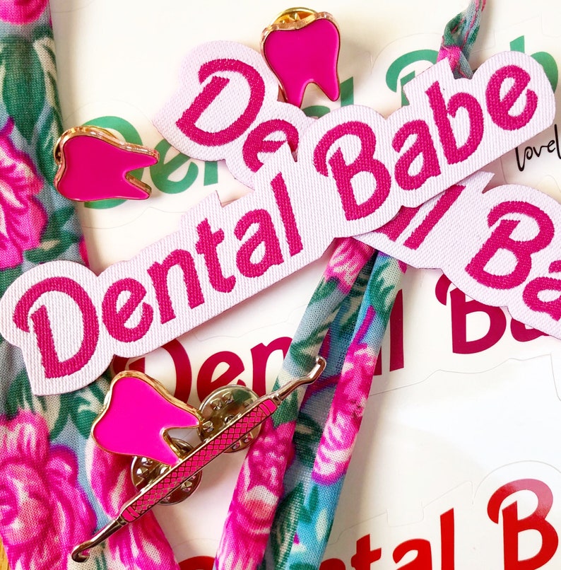 May include: Pink and white fabric patches with the text "Dental Babe" and a pink tooth pin. The patches are on a floral fabric background.