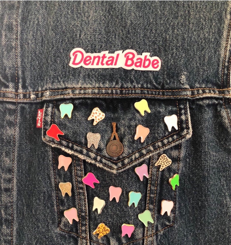 May include: A denim jacket with a pink patch that says "Dental Babe" and a pocket with many colorful tooth pins.