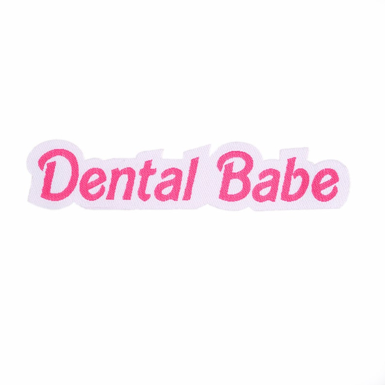 May include: White fabric patch with the text "Dental Babe" in pink cursive lettering.