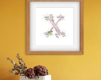 Può includere: Stampa floreale incorniciata della lettera "X" in una cornice di legno. La lettera è composta da fiori rosa, viola e verdi su sfondo bianco. L'opera d'arte è esposta su una parete gialla sopra una mensola di legno con oggetti decorativi.