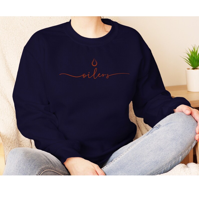 May include: Navy blue sweatshirt with the word "oilers" in a cursive orange font. Above the word is a small orange drop graphic. The sweatshirt is a crew neck style and is made of a soft material.