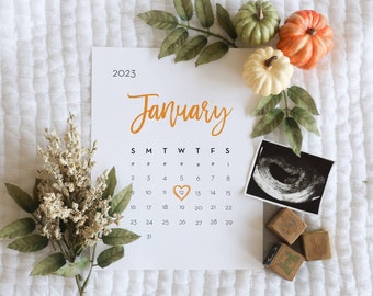 May include: A calendar page for January 2023 with a heart drawn around the 12th. The calendar is surrounded by fall-themed decorations, including gourds, leaves, and wooden blocks.