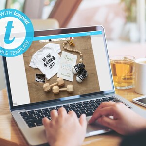 May include: A laptop computer displaying a website with a mockup of a baby onesie with the text "Do you even lift?" and a baby shoe. The onesie is white with black text and a black and white ultrasound image. The baby shoe is black with white trim. The website is on a light blue background with a white border. The laptop is on a wooden table.