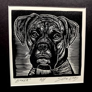 May include: Black and white woodcut print of a Boxer dog's head. The print is signed "Sean Eaby" and titled "Boxer" with the initials "A/P".