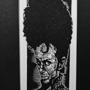 May include: Black and white linocut print of a person with a large afro and a spiral design on their forehead. The print is framed and signed, with the word "PRINCE" and the artist's name visible at the bottom.