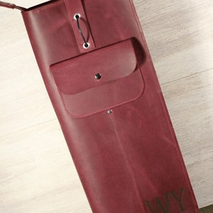 K&ouml;nnte beinhalten: Eine burgunderfarbene Ledertasche mit Rei&szlig;verschluss und einer kleinen Tasche auf der Vorderseite. Die Tasche hat einen Schultergurt und die Initialen "WY" sind auf der Vorderseite gepr&auml;gt.