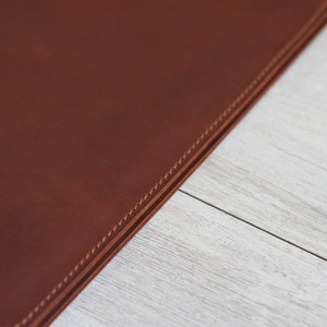 May include: Close-up of a brown leather surface with double stitching along the edge.