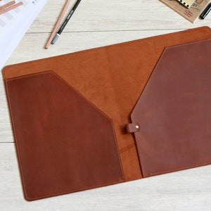 May include: A brown leather folder with two pockets and a flap closure. The folder is open and the inside is lined with a brown suede material.