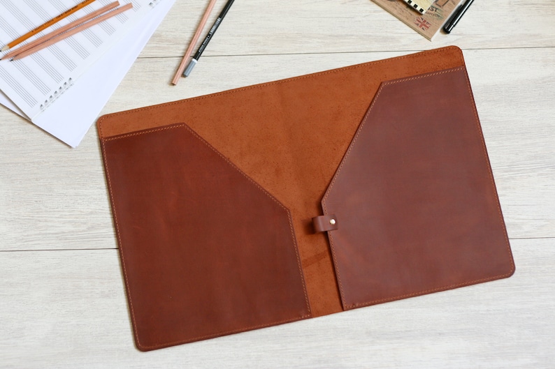May include: A brown leather folder with two pockets and a flap closure. The folder is open and the inside is lined with a brown suede material.