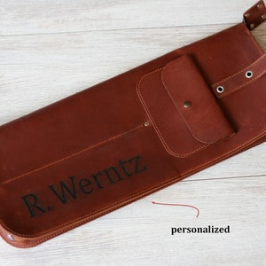 K&ouml;nnte beinhalten: Eine braune Ledertasche mit Rei&szlig;verschluss, einer kleinen Tasche und einem Tragegriff. Die Tasche ist mit dem Namen "R. Werntz" personalisiert.