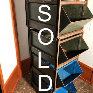May include: A set of four black metal storage bins with blue, green, and black interiors. The bins are stacked on top of each other and have a metal frame.