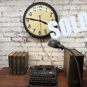May include: A vintage office scene featuring a black typewriter, a large wall clock, a desk lamp, and several antique books. The clock has a cream-colored face with black numbers and hands. The word "SOLD" is overlaid on the image.