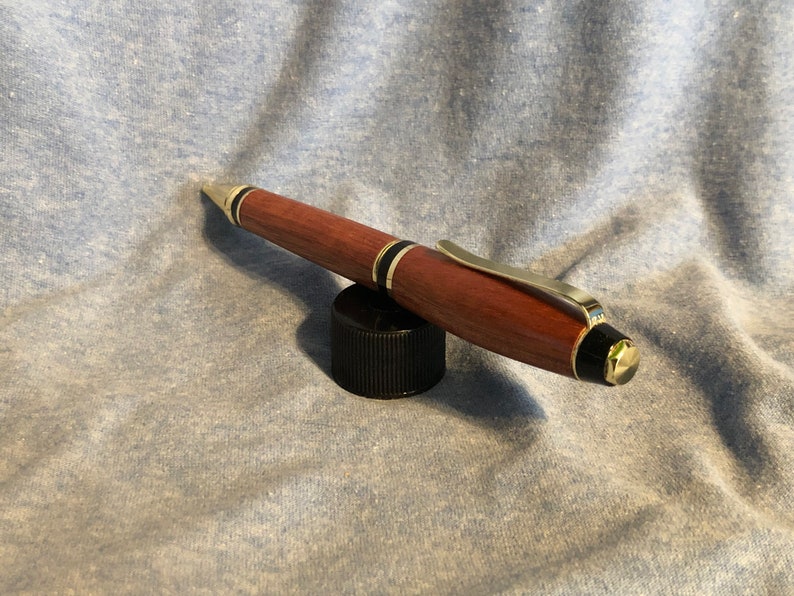 May include: A wooden pen with gold accents and black trim. The pen is resting on a black cap.