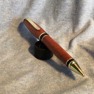 May include: A wooden pen with a gold-colored tip and black accents. The pen is resting on a black cap.