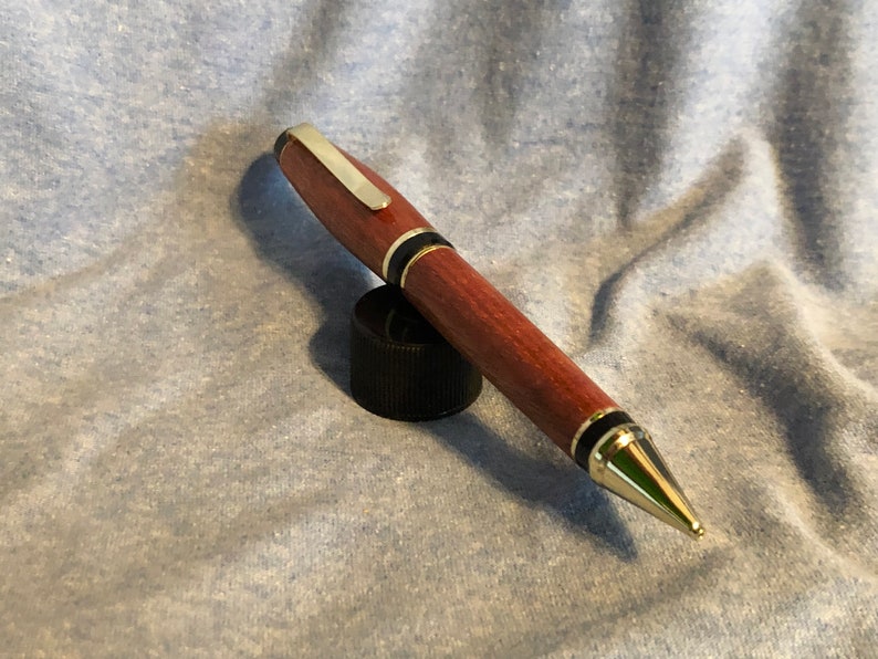 May include: A wooden pen with a gold-colored tip and black accents. The pen is resting on a black cap.
