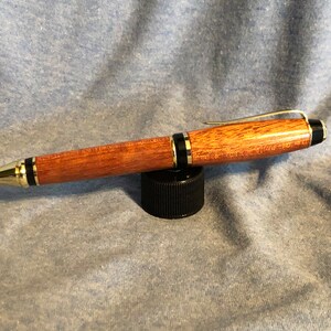 May include: A wooden pen with gold accents and black trim. The pen has a brown wood grain pattern and a gold clip.