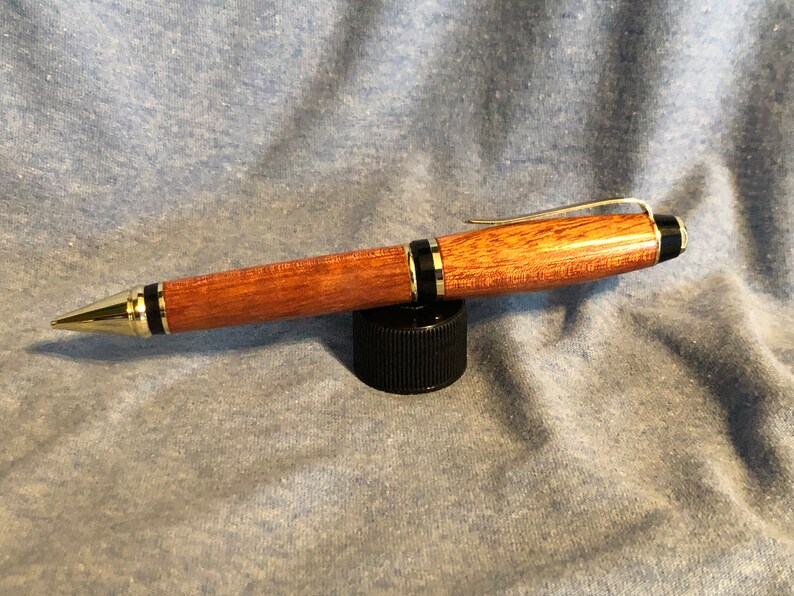 May include: A wooden pen with gold accents and black trim. The pen has a brown wood grain pattern and a gold clip.