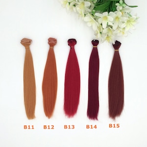 May include: Five bundles of hair extensions in various shades of brown and red, labeled B11, B12, B13, B14, and B15. Each bundle is tied at the top with a band. White flowers are in the background.