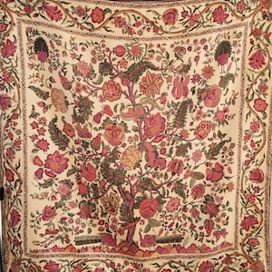 May include: A square textile featuring a cream-colored background with an intricate, multi-colored floral and tree pattern. The design includes various shades of pink, red, and green, with stylized peacocks at the base and corners of the border.