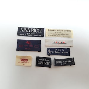 Può includere: Una collezione di otto etichette rettangolari in tessuto per abbigliamento con vari nomi di marchi e loghi, tra cui Nina Ricci, Royal Academy of Arts, Etro, Rodier, Polo by Ralph Lauren, Levi's, Liberty e Pierre Cardin in nero, bianco e crema.