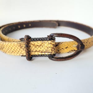 Peut inclure: Une ceinture avec une sangle à motif peau de serpent jaune et noir, dotée d'une boucle en cuir marron foncé et d'un passant assorti. La ceinture présente une série de trous de réglage le long de la sangle et un intérieur marron foncé lisse.