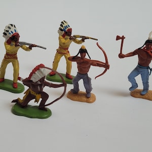 May include: Five plastic toy figurines depicting Native American warriors in various poses. Two figures wear yellow outfits with feathered headdresses and hold rifles, two hold bows and arrows, and one holds a tomahawk while wearing blue trousers.