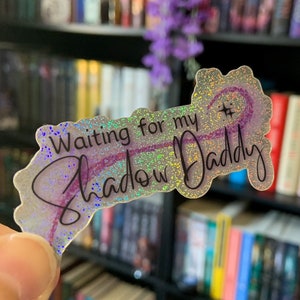 Puede incluir: Una pegatina holográfica con purpurina y el texto "Waiting for my Shadow Daddy" en letra cursiva negra.