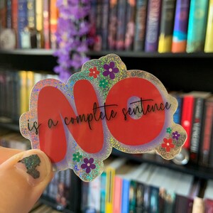 Puede incluir: Una pegatina holográfica con la palabra "NO" en rojo y la frase "is a complete sentence" en escritura negra. La pegatina está decorada con pequeños detalles florales en rojo, morado y verde.