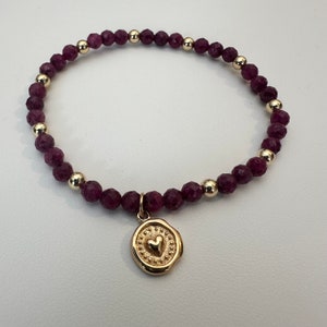 May include: A purple gemstone bracelet with a gold heart charm. The bracelet is made of small, round beads and has a delicate, feminine look.
