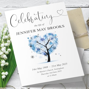 May include: A white card with blue and black snowflakes forming a heart shape around a tree. The text "Celebrating the life of JENNIFER MAY BROOKS" is at the top of the card. The dates "14st May 1969 - 21st May 2025" and "Thursday 2nd June 2025 at 11.00am" are at the bottom of the card.