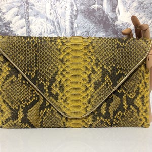 May include: A yellow and black snakeskin clutch bag with a gold-toned clasp.