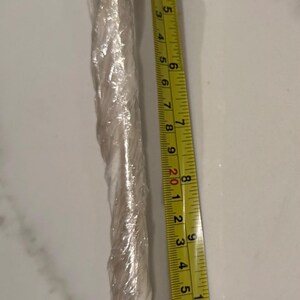 May include: A yellow and black measuring tape showing inches. The tape is next to a clear, wrapped object. The tape measures up to 14 inches.