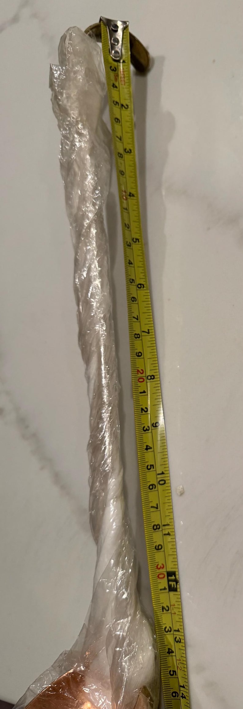 May include: A yellow and black measuring tape showing inches. The tape is next to a clear, wrapped object. The tape measures up to 14 inches.
