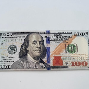 May include: A close-up of a United States one hundred dollar bill. The bill features a portrait of Benjamin Franklin and the text "ONE HUNDRED DOLLARS". The bill is green, black, and white.