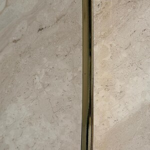 May include: A copper-colored ladle with a long, shiny, silver-colored handle. The ladle's bowl has a hammered texture. The handle curves at the top for hanging. The ladle is designed for kitchen use.