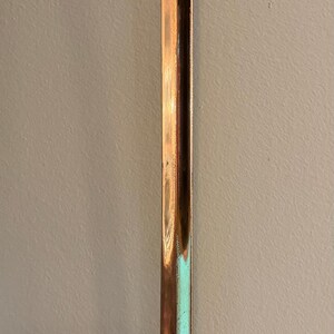 May include: A copper ladle with a hammered bowl and a long, straight handle. The ladle has a shiny, reflective surface and is designed for kitchen use. The handle has a curved hook for hanging.