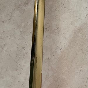 May include: A copper and brass ladle with a long, curved handle. The handle is gold-colored, and the bowl is a shiny copper. The ladle is designed for kitchen use and is likely used for serving soups or sauces.