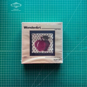 May include: A WonderArt latch hook kit featuring an apple design. The kit includes the materials to create a finished piece approximately 10 x 10 inches. The packaging displays the apple design with a red apple and a white background.