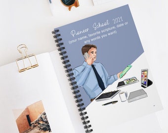 Op de afbeelding: Een blauwe spiraalnotitieblok met de tekst "Pioneer School 2021 (uw naam, favoriete schriftpassage, datum of alle woorden die u wilt)" op de omslag. De omslag toont ook een illustratie van een man aan de telefoon aan een bureau met een laptop, een tablet, een telefoon, een pen en een koffiekopje.